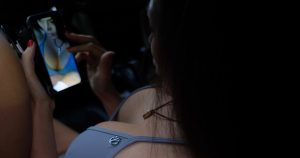 A young woman in a bra looks a a recently taken photo of herself on her cell phone.