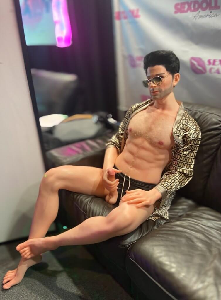 Realistic male sex doll sitting on couch showing his genitals.
